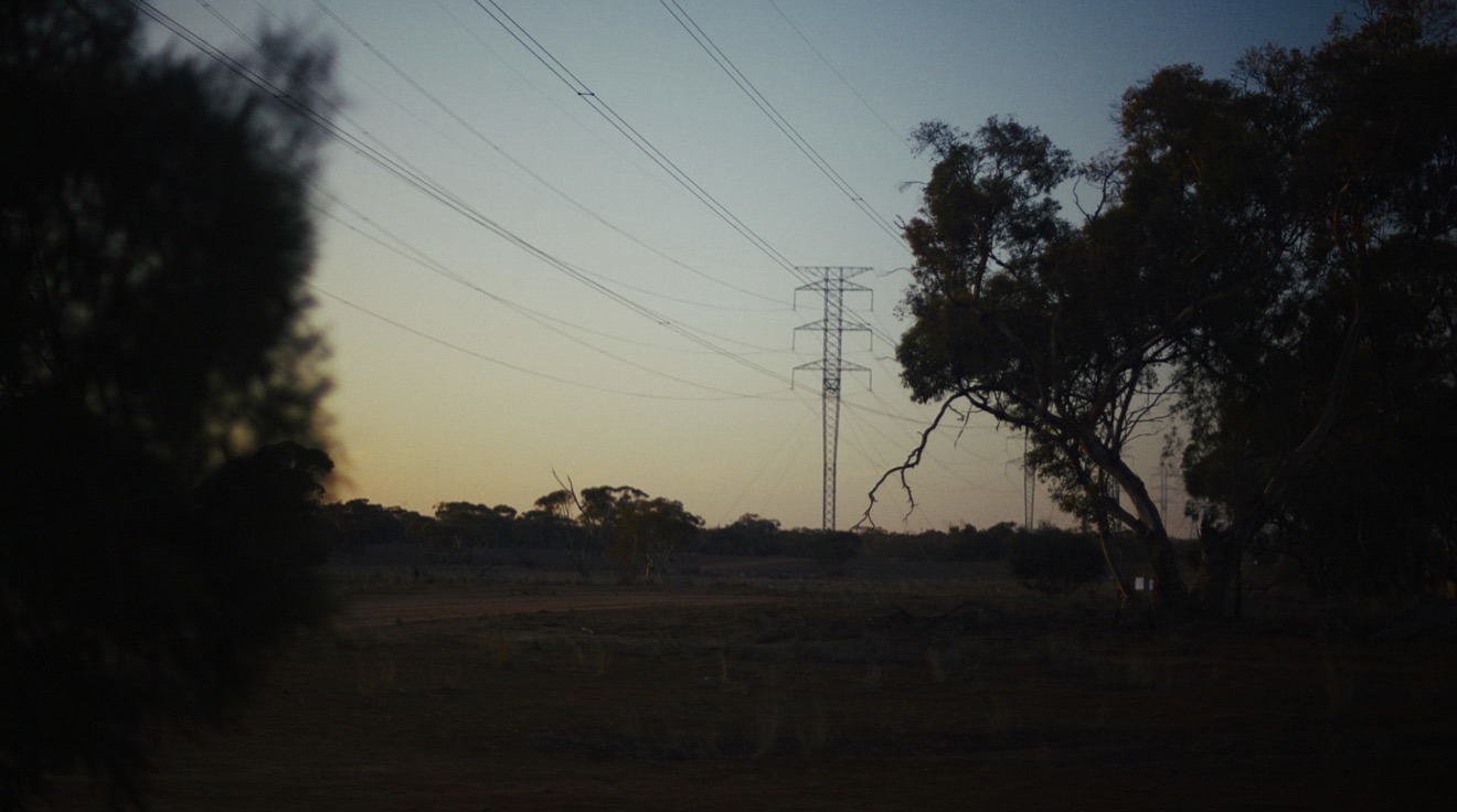 Electricity transmission tower and power lines at dusk over open farmland